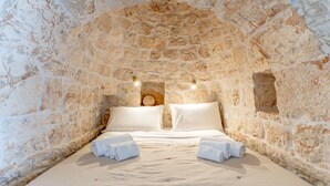 A cozy, stone-walled bedroom with a bed, pillows, and two wall-mounted lights.