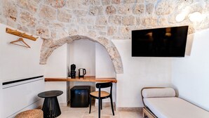 A compact living space with a stone wall, a flat-screen TV, a small kitchenette, a sofa, and a round table.