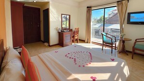 Habitación de hotel con cama, escritorio, silla, televisión y balcón con vistas.