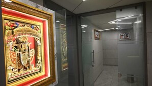 A hallway with a framed artwork on the left, a glass door, and a tiled floor. - HOTEL SKY GOLD (Gandhinagar)