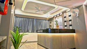 A hotel reception area with a modern design, including a reception desk, a ceiling fan, and a wall-mounted fan. - HOTEL SKY GOLD (Gandhinagar)
