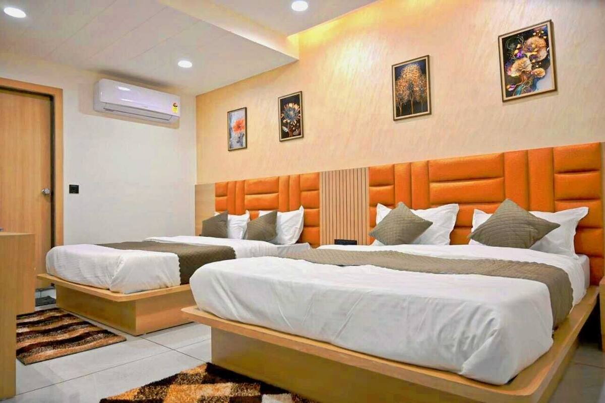 Habitación de hotel con dos camas, cabecero de madera, aire acondicionado de pared y obras de arte en las paredes.