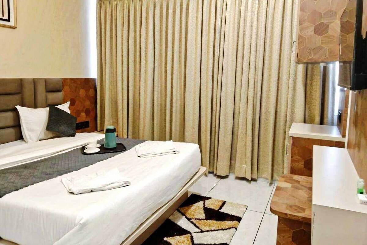 Una habitación de hotel con cama, mesita de noche, televisor y ventana con cortinas.