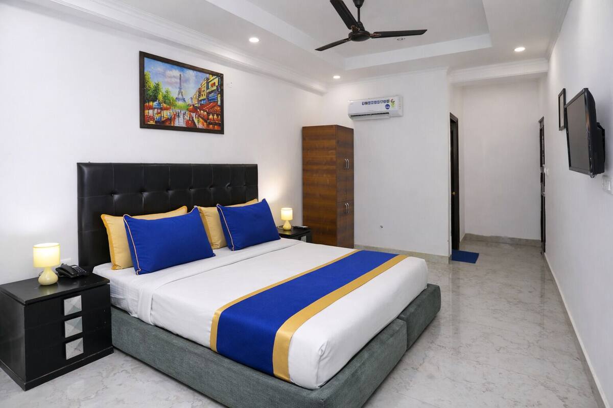 Quarto de hotel com cama, mesa de cabeceira, guarda-roupa, ar condicionado e televisão.