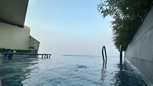 Una piscina infinita con una vista despejada del horizonte, una pared de hormigón en un lado y una estructura metálica en el otro.