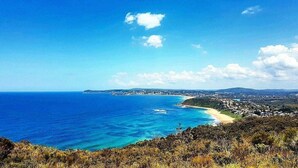 A coastal landscape with a clear view of the ocean, a sandy beach, and a town in the distance.