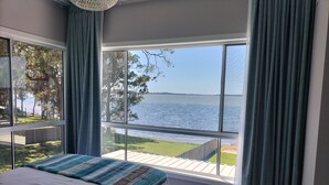 A bedroom with a large window offering a view of a lake and trees.