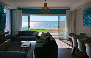 Una sala de estar moderna con un sofá grande, una mesa de centro y un comedor con vistas al mar.