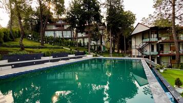 Una piscina con plataforma de borde, rodeada de árboles y edificios modernos.