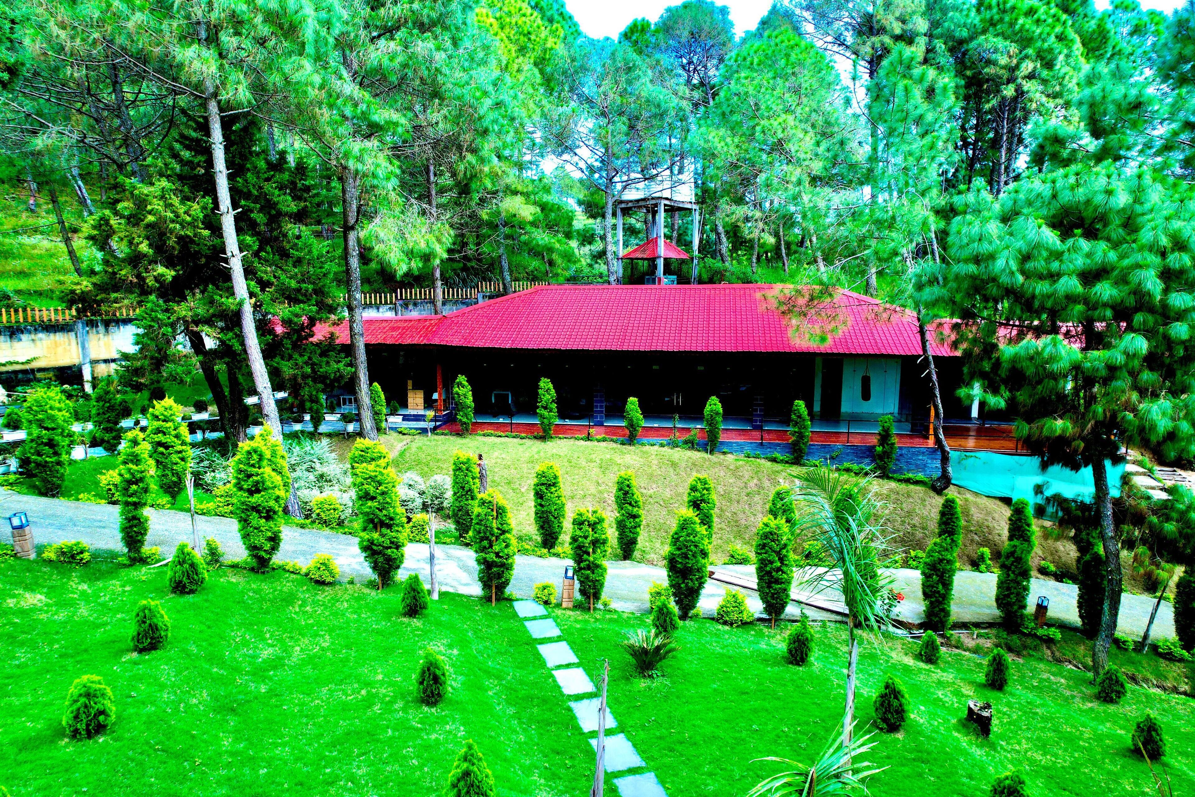 A building with a red roof, surrounded by a well-maintained garden with various trees and shrubs.