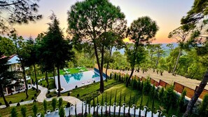 A resort with a swimming pool, manicured lawns, and a variety of trees.
