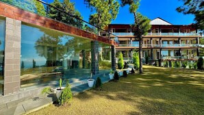 A modern two-story building with large glass windows, a brick facade, and a well-maintained lawn with potted plants. - KUMAON ECO RESORTS (Dwarahat)
