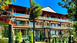 A multi-story building with a modern architectural style, featuring large windows and a balcony on the upper floor. - KUMAON ECO RESORTS (Dwarahat)
