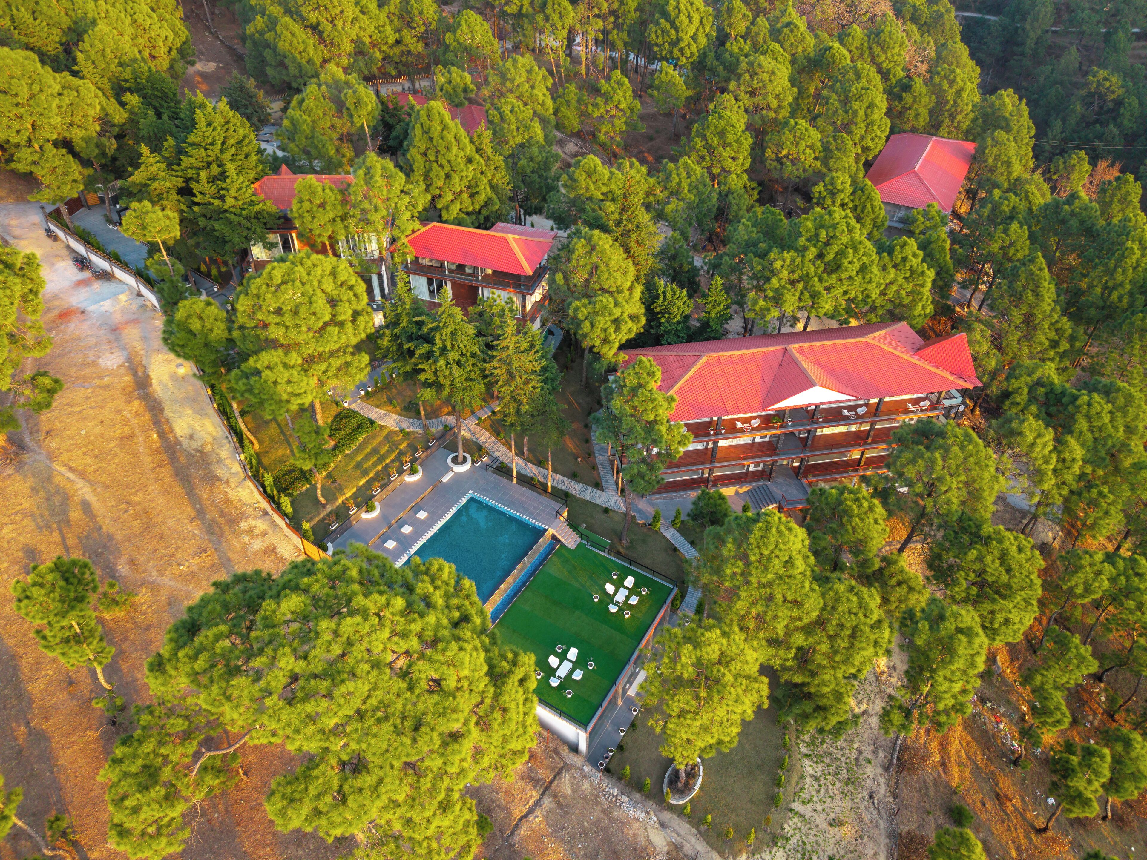 An aerial view of a resort with multiple buildings, a swimming pool, and surrounding forested area.