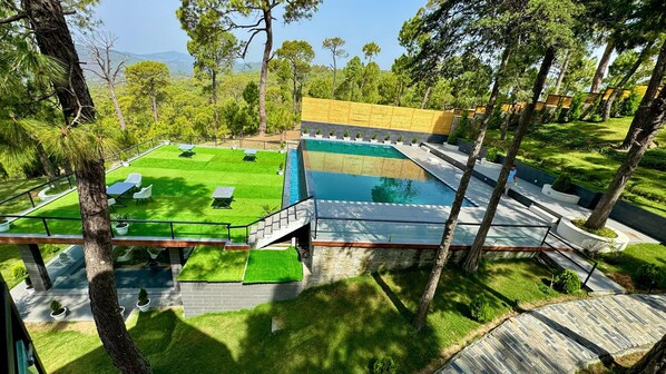 A pool area with a wooden deck, green artificial grass, and a view of the surrounding landscape.