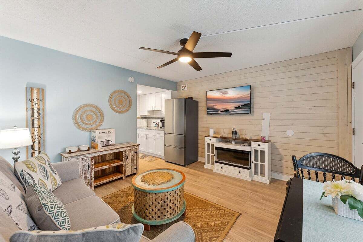 A living room with a sofa, a coffee table, a television, and a kitchen area with cabinets and appliances.