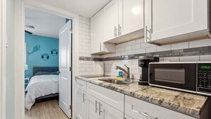A compact kitchen with white cabinets, a granite countertop, a microwave, and a sink. - Beautiful 1BR Condo w/ Ocean View & 2 Heated Pools (North Wildwood)