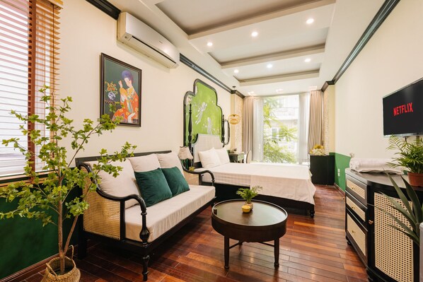 A hotel room with a sofa, a bed, a small table, a TV, and a potted plant.