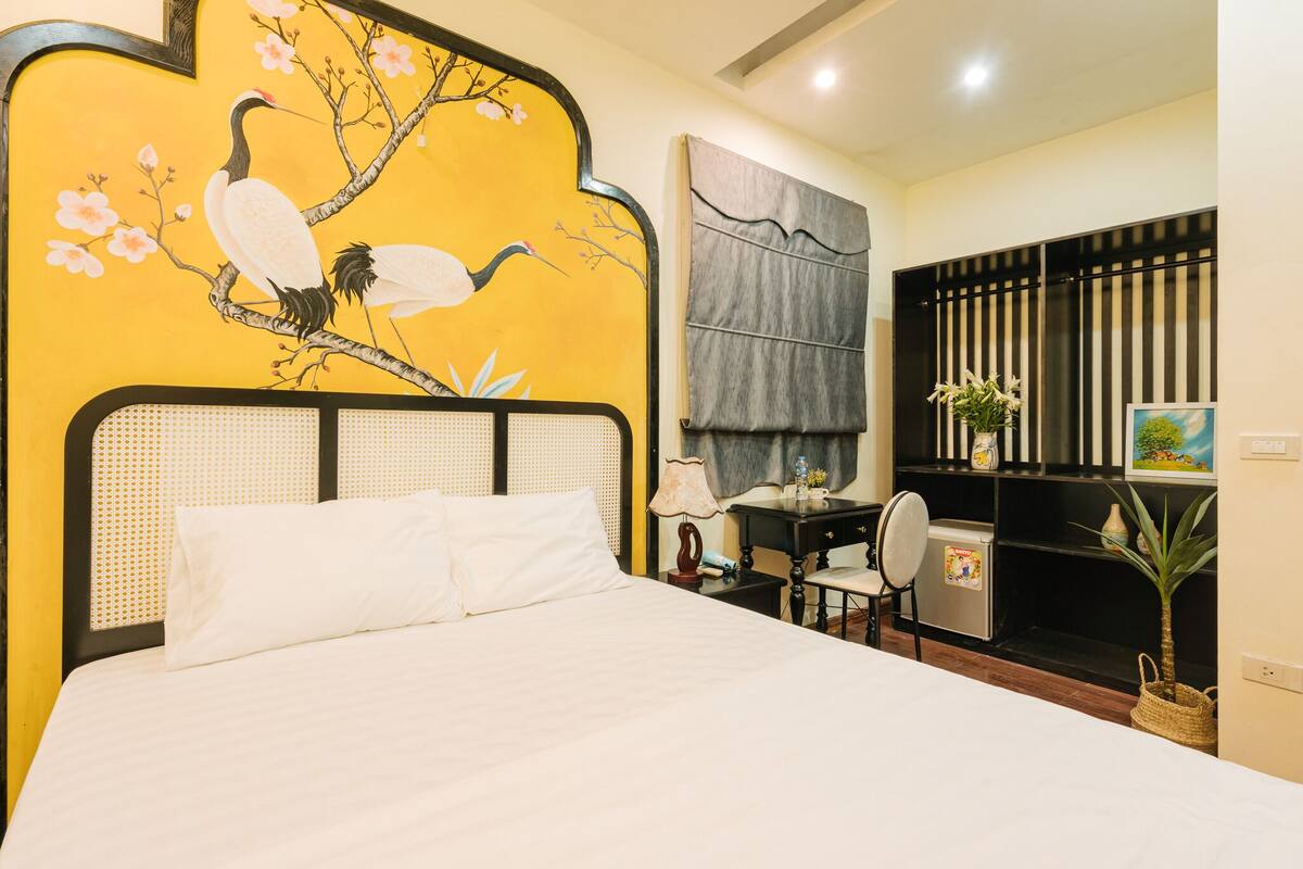 Ein Hotelzimmer mit Bett, Schreibtisch, Stuhl, kleinem Kühlschrank und einer Wand mit Vogel- und Blumenmuster.