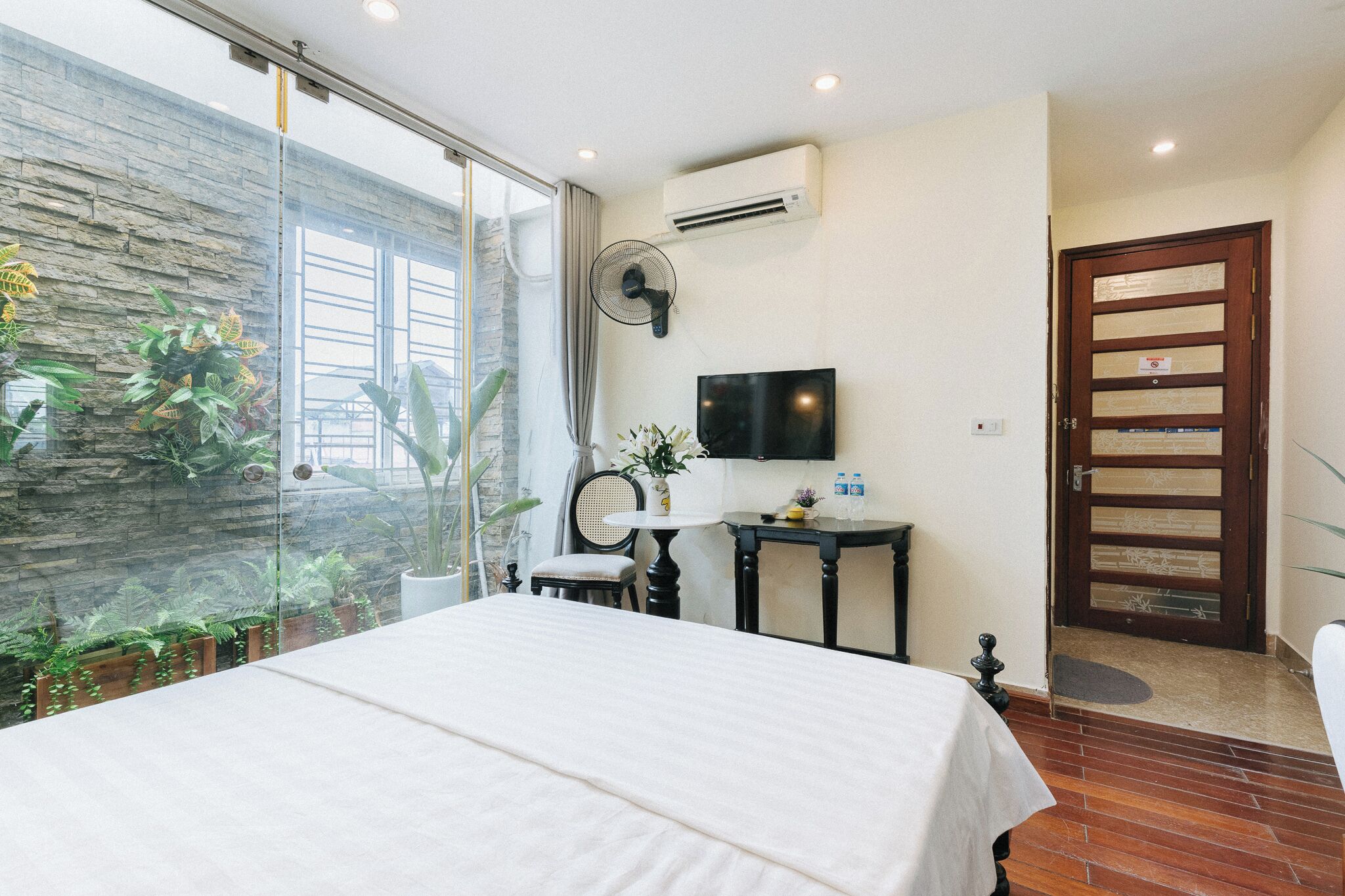 Une chambre avec un grand lit, une télévision, un ventilateur et une porte dotée d’un panneau en verre.