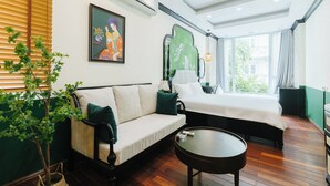 A hotel room with a sofa, a bed, a round table, a potted plant, and a painting on the wall. - Sun Clover Boutique Hotel (Hanoi)