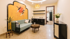 A modern living room with a sofa, coffee table, and decorative plants. There is a wall-mounted shelf and a cabinet with a woven front. - Sun Clover Boutique Hotel (Hanoi)