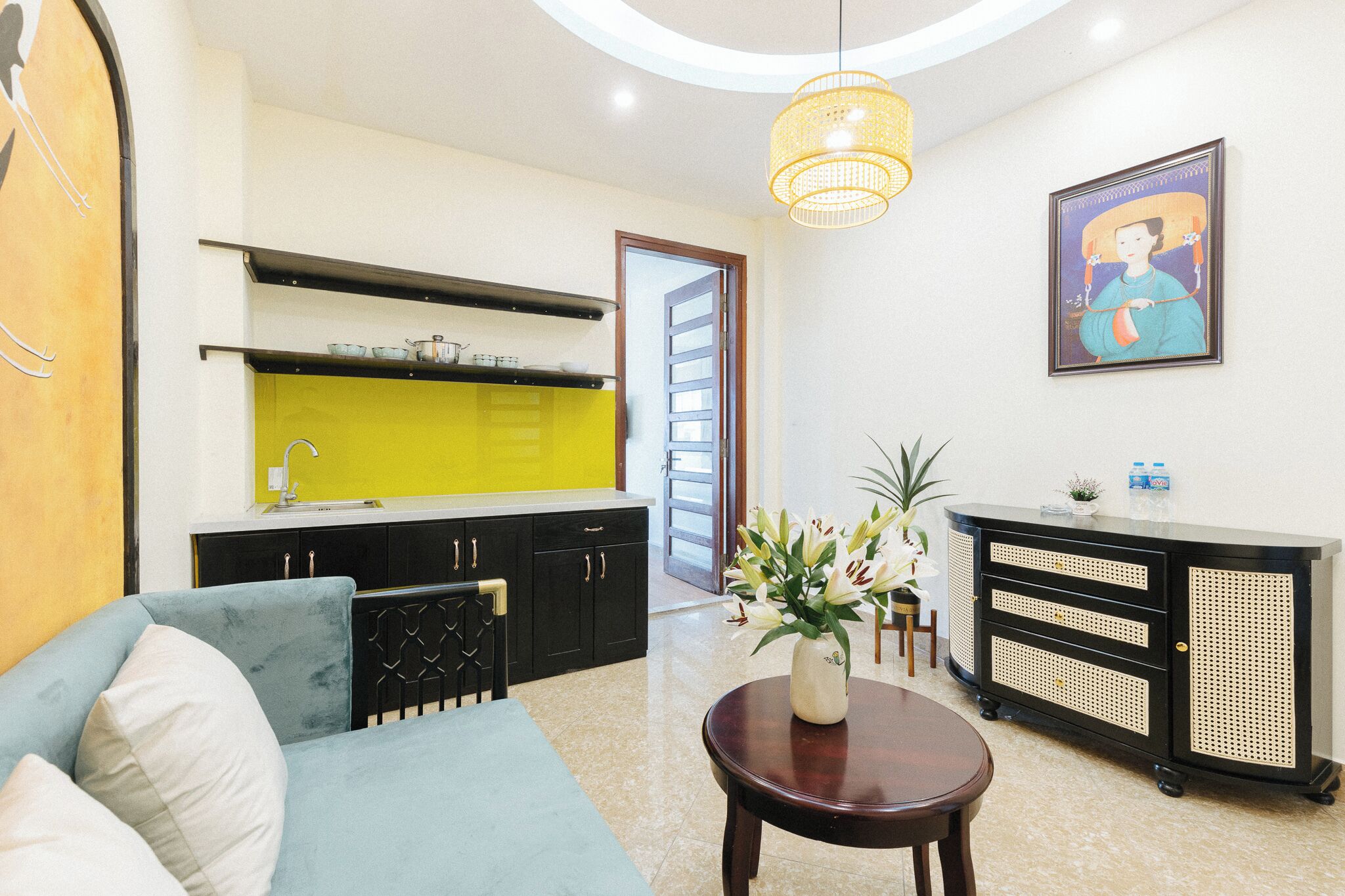 A modern living room with a sofa, a dining table, and a kitchen area with a yellow backsplash.