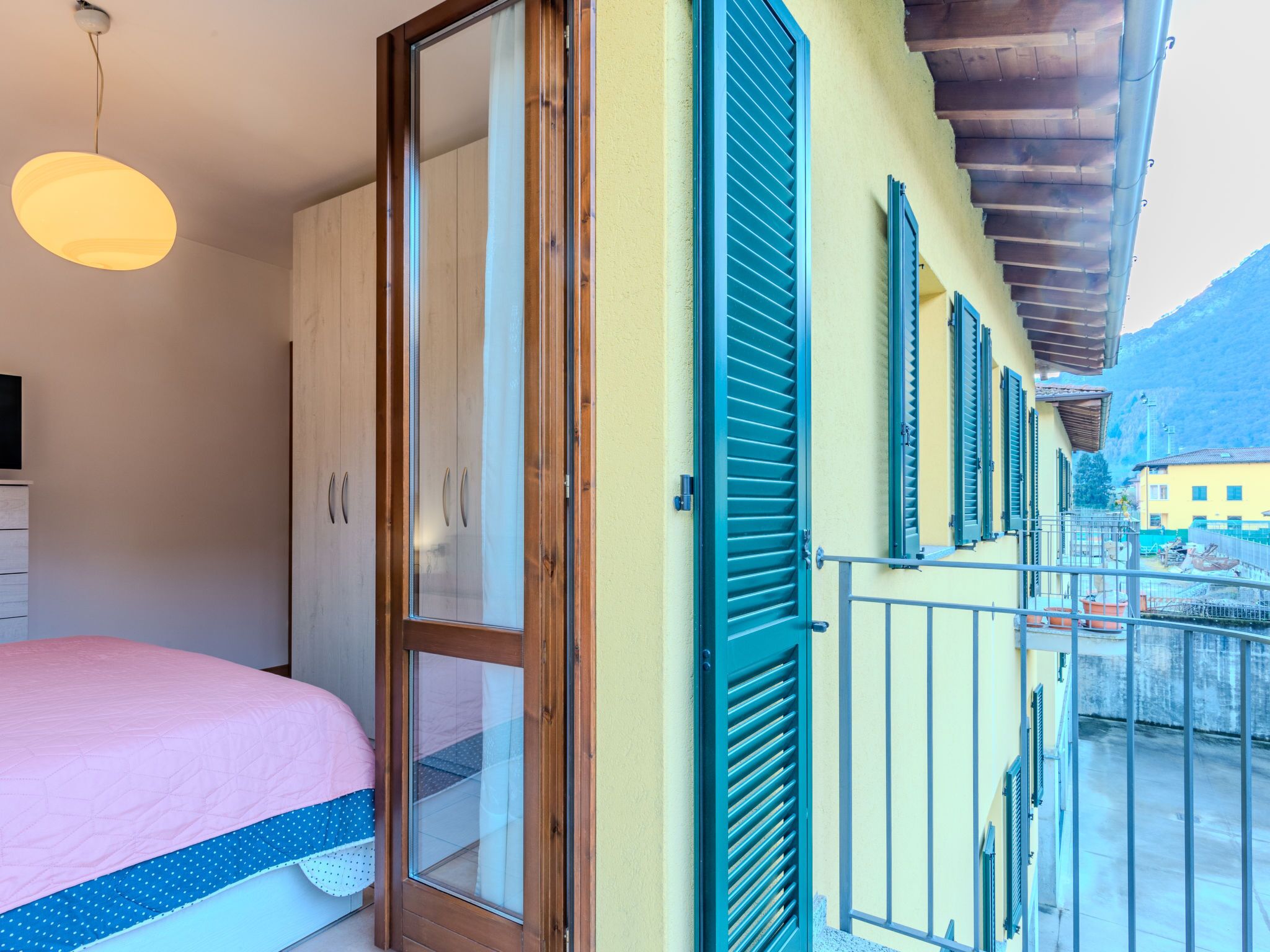 Quarto com cama, guarda-roupa e varanda com vista para a cidade.