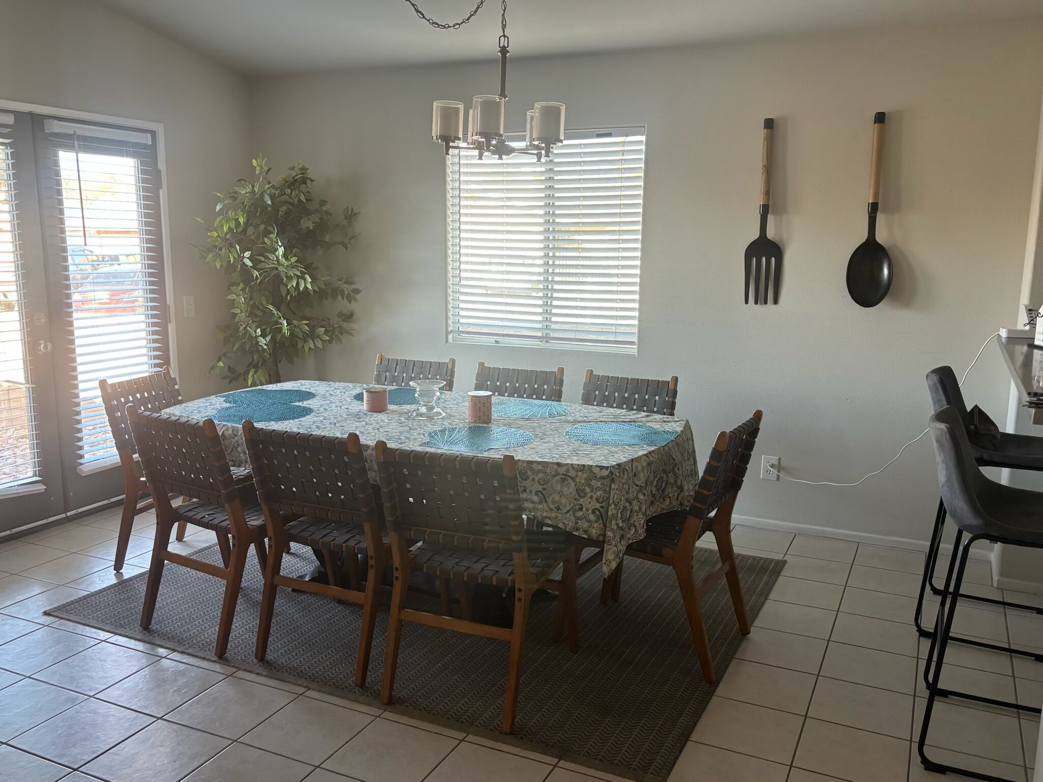 A dining area with a round table, six chairs, a chandelier, a potted plant, and a sliding glass door.