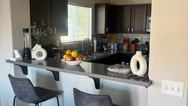 A modern kitchen with two bar stools, a central island, and dark cabinetry.