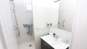 A modern bathroom with a glass shower enclosure, a white sink with a mirror above it, and a small shelf with plants. - St Cyprien: An enchanting interlude on the marina (Saint-Cyprien)