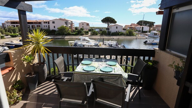 A balcony with a table set for four, overlooking a marina with boats and buildings in the background. - St Cyprien: An enchanting interlude on the marina (Saint-Cyprien)