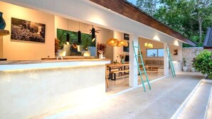 A modern kitchen with a long countertop, pendant lights, and a stone wall. - Mateo Villa Uluwatu  (Pecatu)