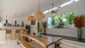 A modern kitchen with wooden furniture, pendant lights, and a large window overlooking greenery. - Mateo Villa Uluwatu  (Pecatu)