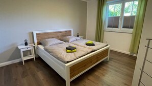 A bedroom with a wooden bed, two bedside tables, a window with curtains, and a view of greenery outside.