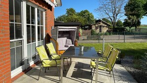 An outdoor patio with a table and chairs, a wicker sofa, and a brick building with large windows.