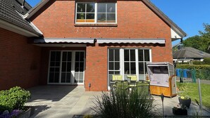 A two-story brick house with a covered patio, large windows, and a small garden area.