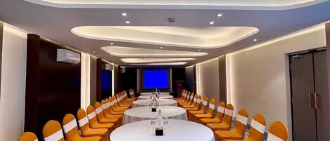 A conference room with a round table, multiple chairs, and a television screen.