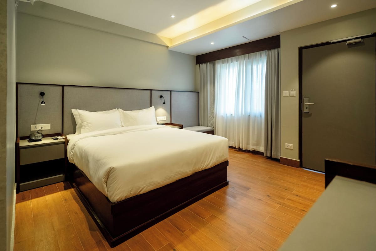 Ein modernes Hotelzimmer mit einem großen Bett, Holzboden, einem Nachttisch mit Lampe und einem Fenster mit Vorhängen.