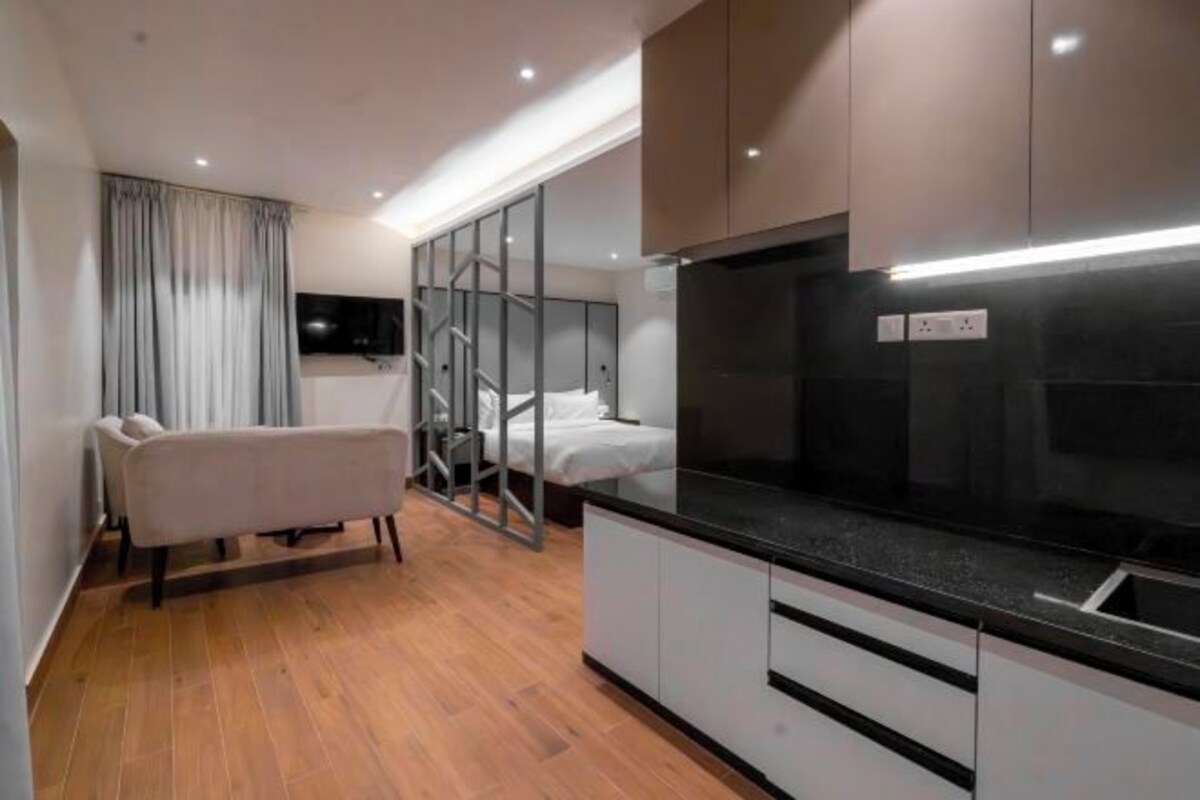 A modern bedroom with a bed, a bench, a TV, and a kitchenette.