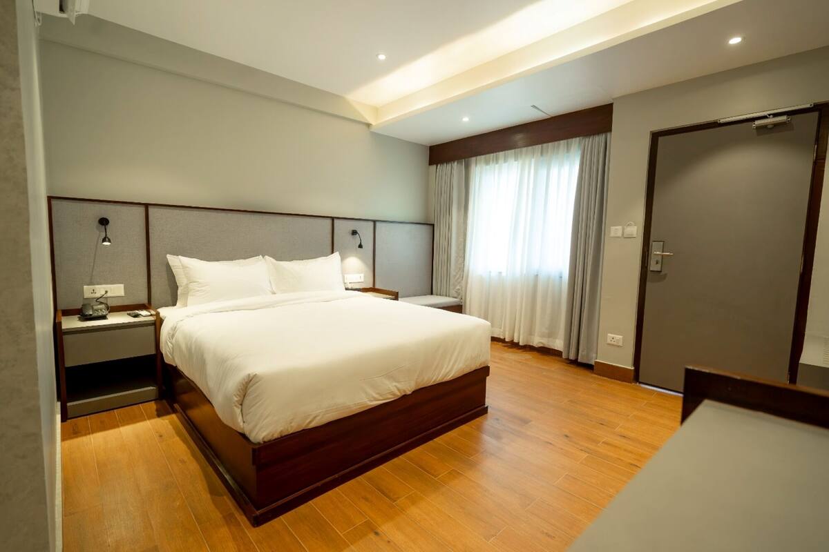 Ein modernes Hotelzimmer mit einem großen Bett, Holzboden, einem Nachttisch mit Lampe und einer Tür.