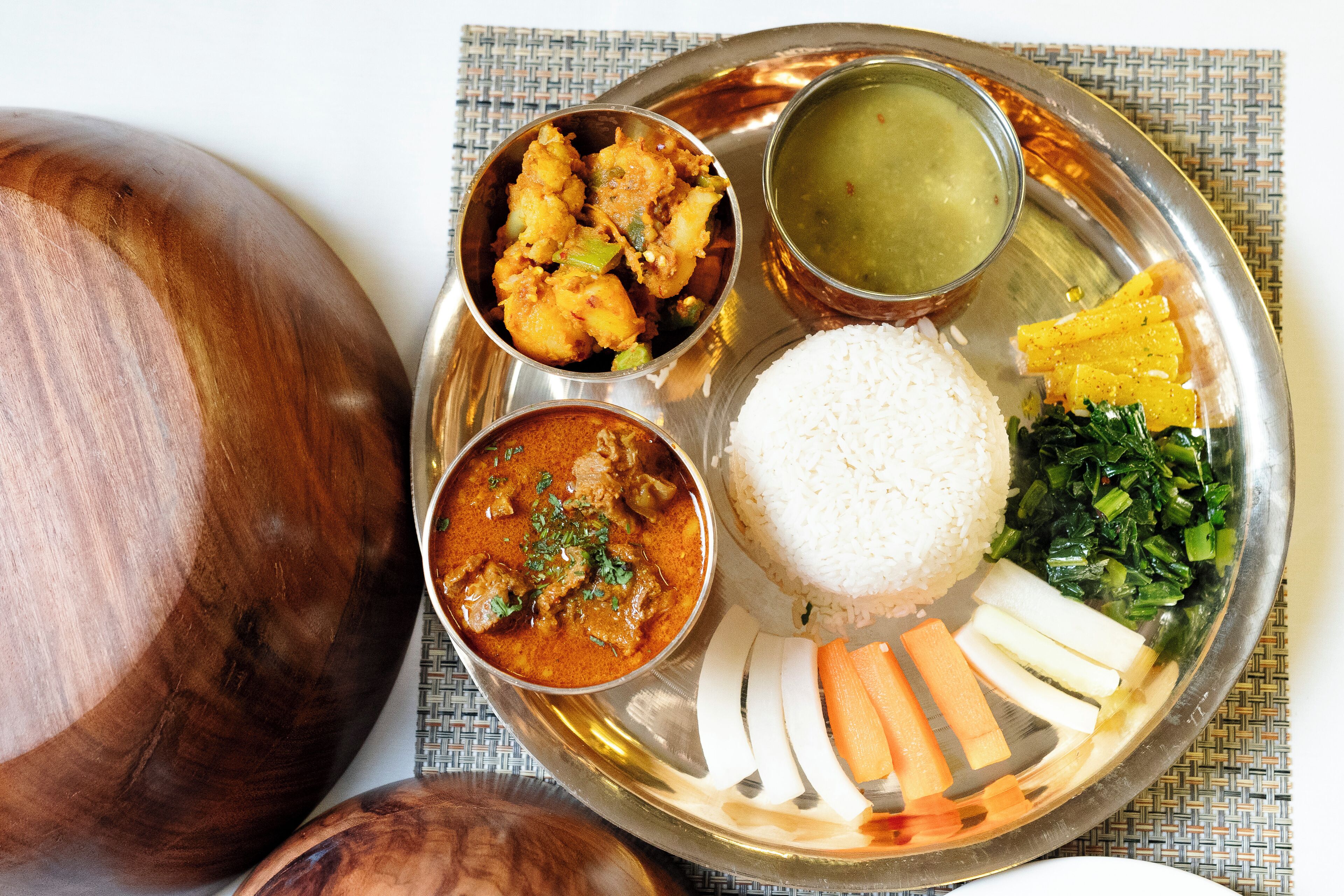 Comida tradicional india servida en un plato de acero inoxidable con arroz, curry y diversos vegetales.