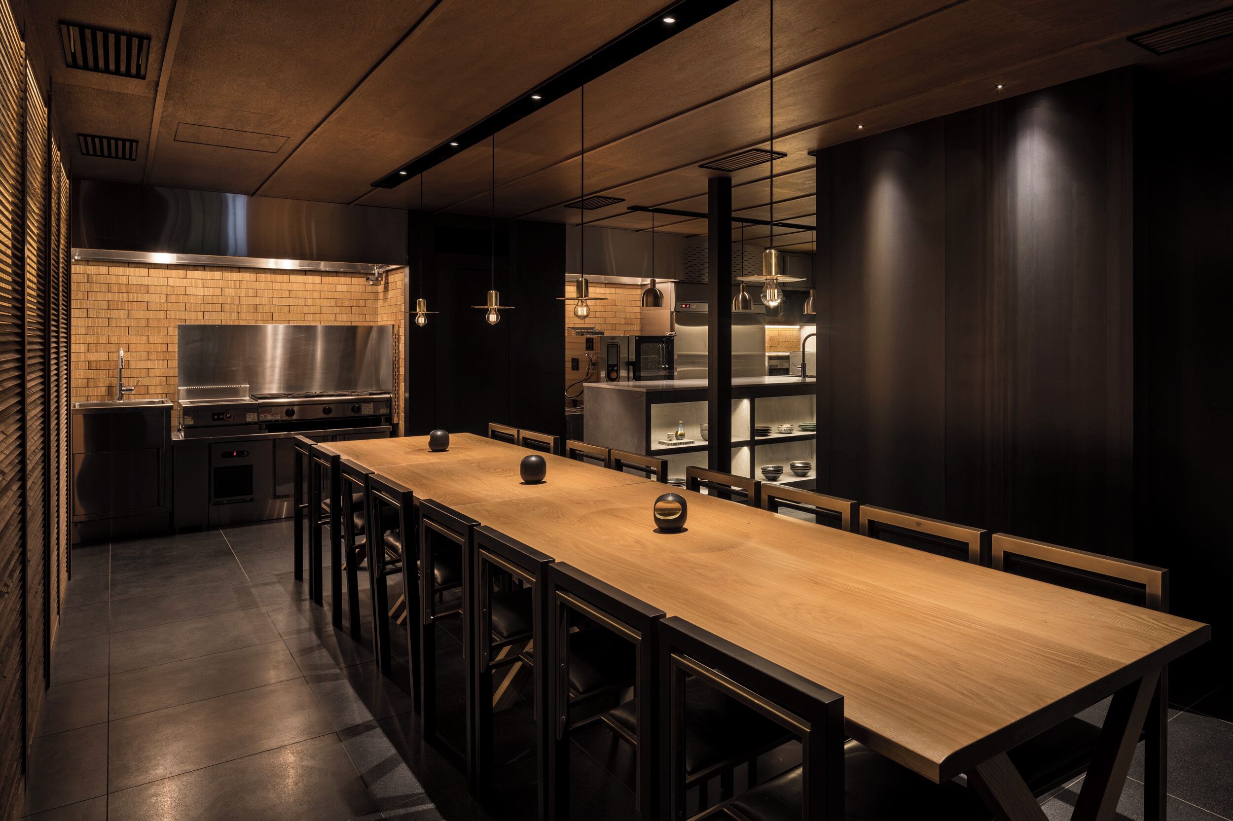 Une cuisine moderne avec une longue table et des chaises en bois, des appareils en acier inoxydable et des luminaires suspendus.