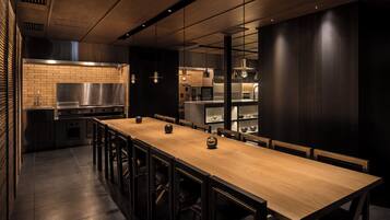 Une cuisine moderne avec une longue table et des chaises en bois, des appareils en acier inoxydable et des luminaires suspendus.