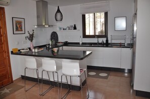 Una cocina moderna con una isla central, taburetes blancos y un ventanal que proporciona luz natural.