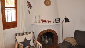 Ein gemütliches Wohnzimmer mit Kamin, einem gestreiften Sessel, einer Couch und einem Fenster mit Vorhängen.