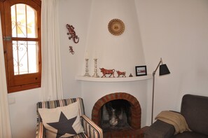 Una sala de estar acogedora con chimenea, un sillón a rayas, un sofá y una ventana con cortinas.