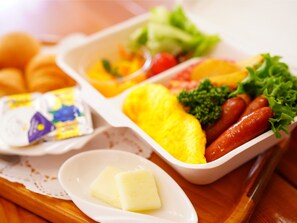 A meal tray with various food items including sausages, vegetables, and a slice of bread.