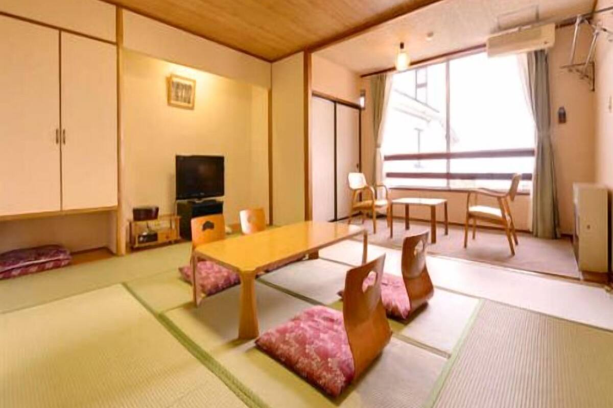 A traditional Japanese room with tatami flooring, a low table, chairs, a television, and sliding doors.