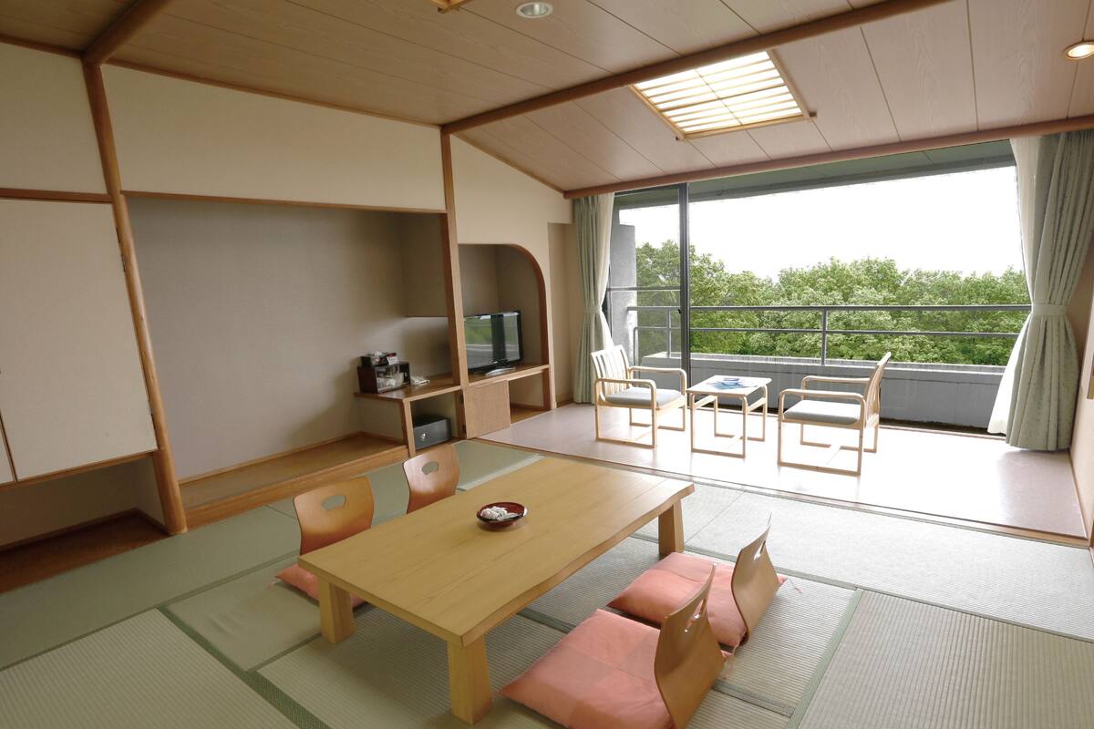A traditional Japanese-style room with tatami flooring, a low wooden table, and a television on a shelf.